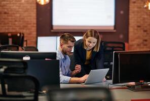 Business colleagues, a man and a woman, engage in discussing business strategies while attentively gazing at a computer monitor, epitomizing collaboration and innovation photo