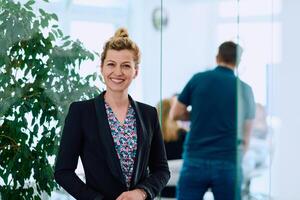 Portrait of a Blonde Businesswoman in a Modern Office with Her Workspace and Colleagues in the Background. photo