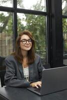 Young woman in eyeglasses working with laptop while sitting at cafe photo