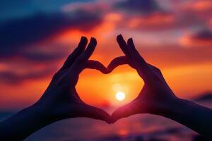 A heart shape formed with hands against a vibrant sunset. Photo conveys love, hope, and the beauty of nature.