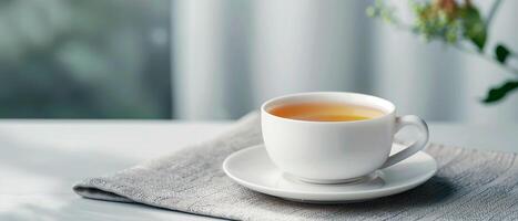 A serene morning moment with a cup of hot tea on a white table, accompanied by a soft gray cloth and natural light. Perfect for relaxation. photo