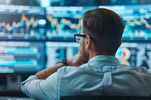 Man analyzing stock market data on multiple computer screens for financial investments and trading decisions, seen from behind. photo