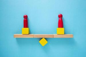 Conceptual image of balance and equality, represented by two red figures balancing on a wooden seesaw photo