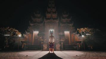 Person in traditional attire in front of illuminated ancient temple at night video