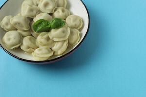 Dumplings in a bowl with a basil leaf on a blue background with space for copyspace text. The concept of national food photo