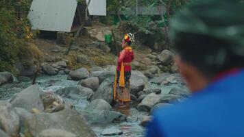 Person in traditional attire standing on rocks in a stream video