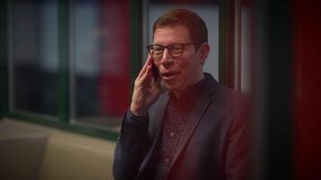 A businessman is gleeful while engaged in a phone conversation inside a contemporary office setting video