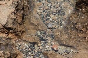 Top view on Calm transparent water surface, above view of underwater pebble. Clear crystal blue sea water and rocky, stone seabed background, texture. photo