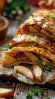 Appetizing golden brown baked strudel with apples and golden puff pastry crust cut into pieces close-up. Vertical image of baked goods photo