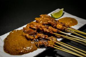 Sate ayam or chicken satay one of the most popular Indonesian dishes, is served with peanut sauce, chili sauce and lime. Usually eaten with lontong or white rice. Selective focus. photo