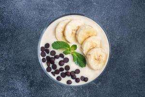 Healthy breakfast, dessert with milk yogurt banana and chocolate on a plate. Dark concrete background. Top view, copy space. photo
