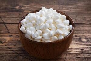 Fresh cottage cheese grain in a wooden bowl. Curd in granules with cream. Wooden rustic background. Copy space. photo