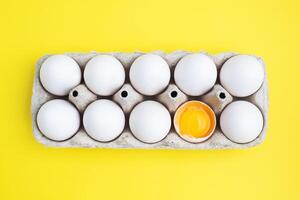Fresh chicken eggs in a package, raw eggs in a white shell in a box. Top view copy space, Yellow background. Broken egg with yolk. photo
