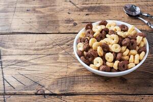 Dry breakfast cereals. Chocolate and corn rings made from natural cereals with milk in a plate. Wooden rustic background, copy space. photo