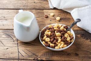 Dry breakfast cereals. Chocolate and corn rings made from natural cereals with milk in a plate. Wooden rustic background, copy space. photo