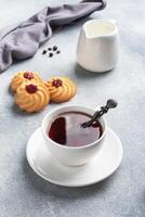 Kurabye shortbread cookies with berry jam in a plate and a cup of tea. Delicious dessert, gray concrete background with copy space. photo