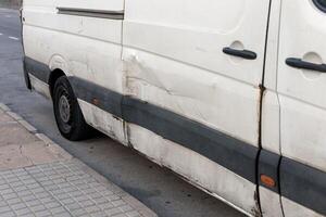 Detailed close-up of a white car with visible damage on its side, featuring dents and scratches. Perfect for showcasing the need for vehicle repairs, insurance case studies, and urban driving risks. photo