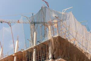 New building construction process. Safety nets and structural beams highlight ongoing work. Detailed shot of multi-level architecture. Ideal for articles on urban development, real estate investment. photo