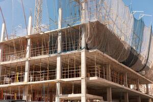 New building construction process. Safety nets and structural beams highlight ongoing work. Detailed shot of multi-level architecture. Ideal for articles on urban development, real estate investment. photo
