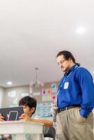 Teacher in class teaching student how use a laptop. photo