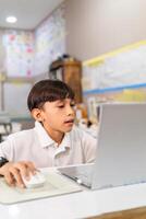 Portrait of Latin american child using a laptop with a mouse in a classroom. photo