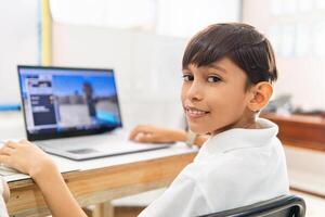 Portrait of Latin american elementary boy using a laptop in class. Technology concept. photo