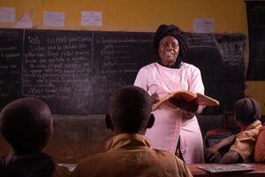 Black female teacher stands in front, explains the lesson by reading from the book from the desk photo