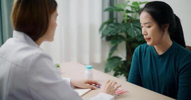 Handheld high angle view shot, Asian doctor explaining how to take medicine to young female patient in clinic office, Health and medicine consultant video