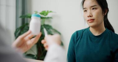 Handheld selective focus shot, Asian doctor explaining how to take medicine to young female patient in clinic office, Health and medicine consultant, Conversation about healthcare video