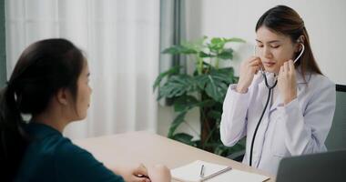 Handheld high angle view shot, Asian doctor use stethoscope on chest of young female patient to check and listening her heartbeat in clinic office, Health and medicine consultant video