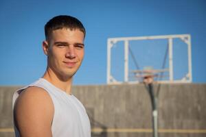 A smiling basketball player on a basketball court with a hoop behind him photo