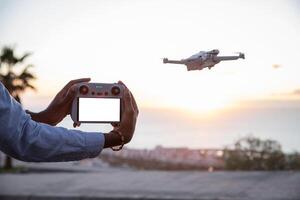 Close up on drone remote control with blank screen for mockup, drone flying beside. photo