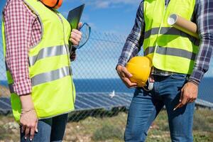 Close-up of the bodies of two engineers wearing reflective vest and holding work tools photo