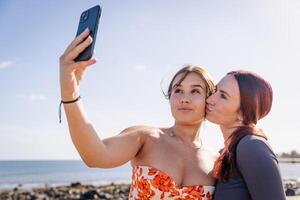 Two sisters take a selfie at the beach and one gives a kiss to the other on the cheek photo