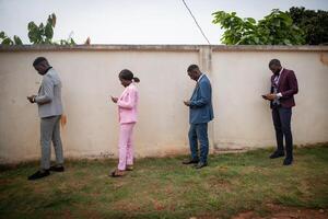 a group of well-dressed young Africans use their smartphones in line while keeping a safe distance during the pandemic. photo