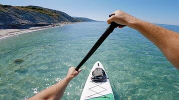 Men rowing on SUP board on transparent sea. First person view of stand paddle boarding in summer. video