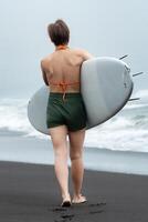 Rear view of unrecognizable woman surfer walking on sand beach with surfboard in hand. Background is filled with soothing sound of sea waves, creating perfect summer beach holiday atmosphere photo