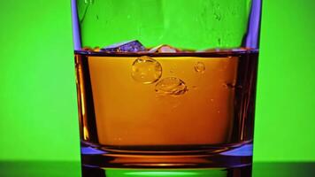 A glass of whiskey with ice cubes being swirled. Green screen backdrop. Warm, soft lighting to create an elegant ambiance. video