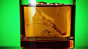 A glass of whiskey with ice cubes being swirled. Green screen backdrop. Warm, soft lighting to create an elegant ambiance. video