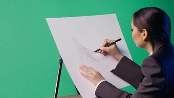 A fashion designer in a stylish outfit, sketching designs. Green screen backdrop. Soft, diffused lighting to reflect a design studio. video