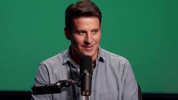 A radio host in casual attire, speaking into a microphone. Green screen backdrop. Soft, ambient lighting to reflect a studio environment video
