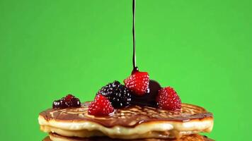 A hand drizzling chocolate syrup over a stack of fluffy pancakes topped with fresh berries. Green screen backdrop. Soft, diffused lighting to create a breakfast feel. video