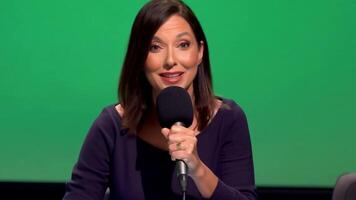 A woman radio host in casual attire, speaking into a microphone. Green screen backdrop. Soft, ambient lighting to reflect a studio environment video