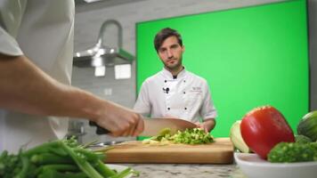 A professional chef in a pristine white uniform chopping vegetables on a kitchen counter. Green screen backdrop. video