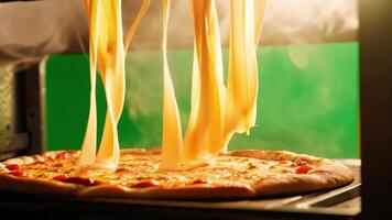A pizza being pulled out of the oven with melted cheese stretching. Green screen backdrop. Warm, soft lighting to evoke an inviting atmosphere. video