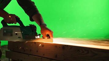 A carpenter in work clothes, using a saw. Green screen backdrop. High contrast lighting to emphasize details. video
