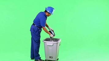 A janitor in uniform, emptying a trash bin. Green screen backdrop. Soft, even lighting to mimic indoor conditions. video