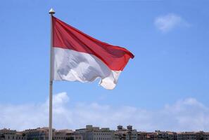The flag of Monaco waving in the wind in front of a blue sky photo
