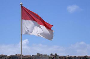 The flag of Monaco waving in the wind in front of a blue sky photo