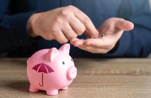 A man counts money and a piggy bank with an umbrella pattern. A man is saving money for insurance. Saving money on insurance services. Receiving compensation. photo